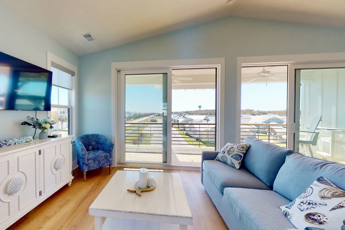 A cozy living area with a plush sofa, coffee table, and a flat-screen television, filled with natural light from sliding glass doors. The space signals relaxation, togetherness, and entertainment options for all ages.