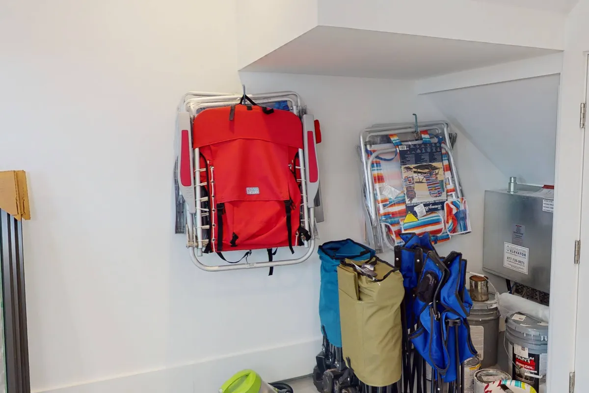 This image shows practical storage in the garage, with colorful beach chairs, a red folding chair, and storage bins neatly organized along the walls. The setup emphasizes easy access to beach equipment, underscoring the home's readiness for spontaneous outdoor fun.