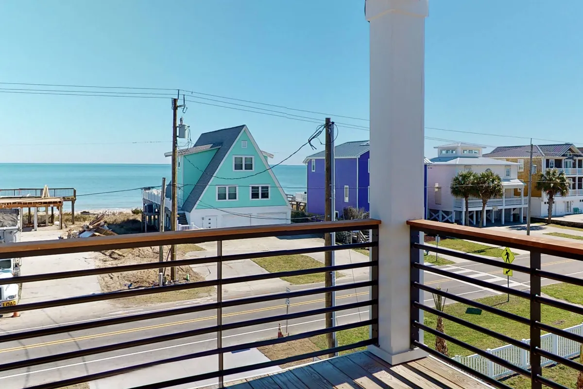 A sweeping ocean view with colorful beach houses and palm trees, this image captures the allure of the coastal landscape visible from the home. The scene suggests a serene atmosphere ideal for outdoor dining or sunset viewing from a deck or balcony.