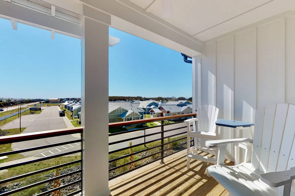 A serene image of a balcony with chairs overlooking the neighborhood, featuring a sturdy railing and open views. The accessible outdoor living space suggests comfortable communal relaxation and easy movement between interior and exterior areas.