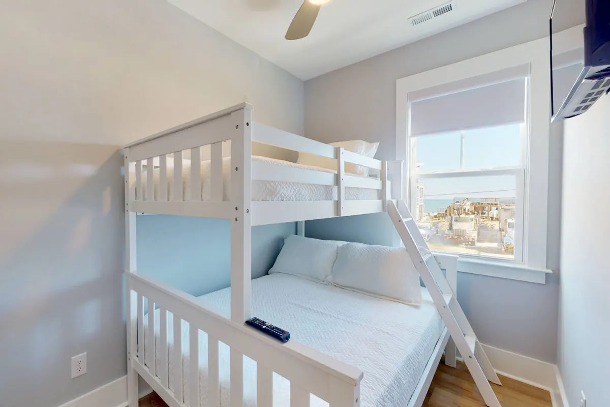 A welcoming bunk room featuring a sturdy bunk bed with crisp linens, a large window letting in ample daylight, and playful accents that create a cozy environment perfect for children or families. The setup invites quiet mornings or bedtime reading.
