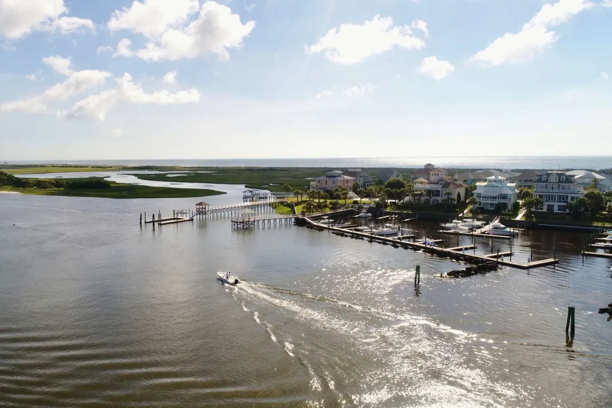 A tranquil river scene with boats docked near waterfront homes and a wooden dock, set against a backdrop of lush greenery. The image conveys opportunities for boating, fishing, and relaxing by the water—key activities highlighted in the content.