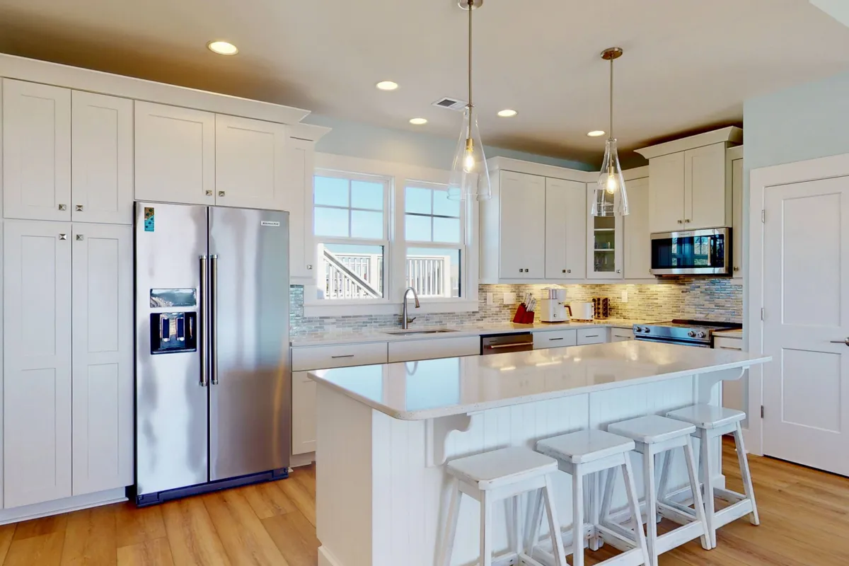 A modern kitchen space centered around a large island, with sleek stainless steel appliances and abundant cabinetry. Sunlight pours in through the window, highlighting a cheerful, functional area ideal for both group feasts and casual breakfasts.